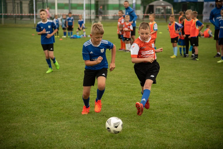 Dwaj młodzi piłkarze w dynamicznym sprincie do piłki na zielonej murawie podczas turnieju